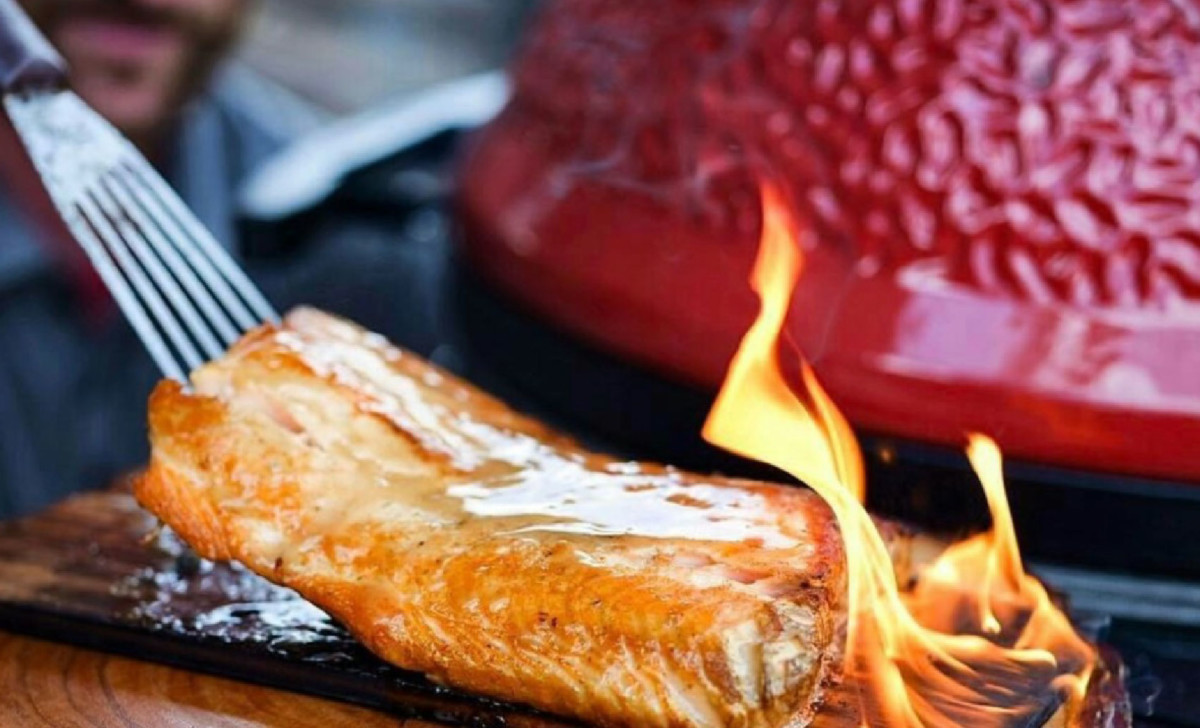 Salmon on cedar plank next to Kamado Joe grill with flame